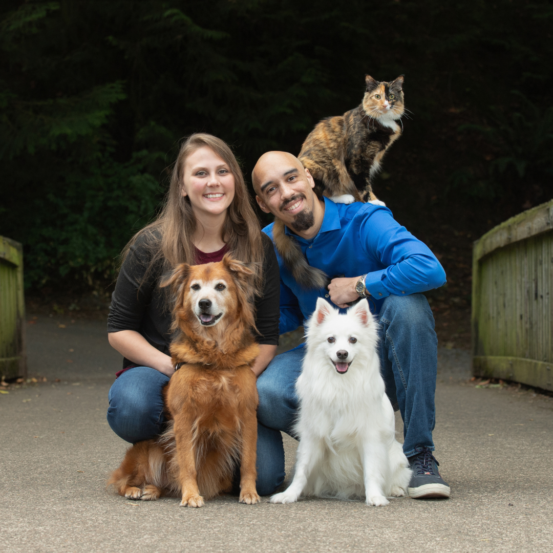 The Luminous Pets family photo, Josie (Founder) with Isiah (Co-owner) with two dogs and a cat on Isiah's shoulder